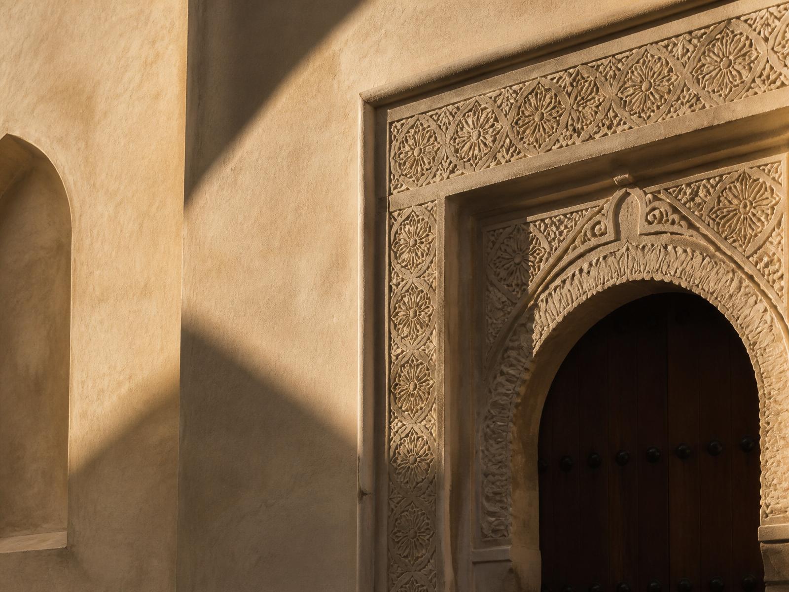 Warm golden light rakes across a carved limestone arch in Muscat.
